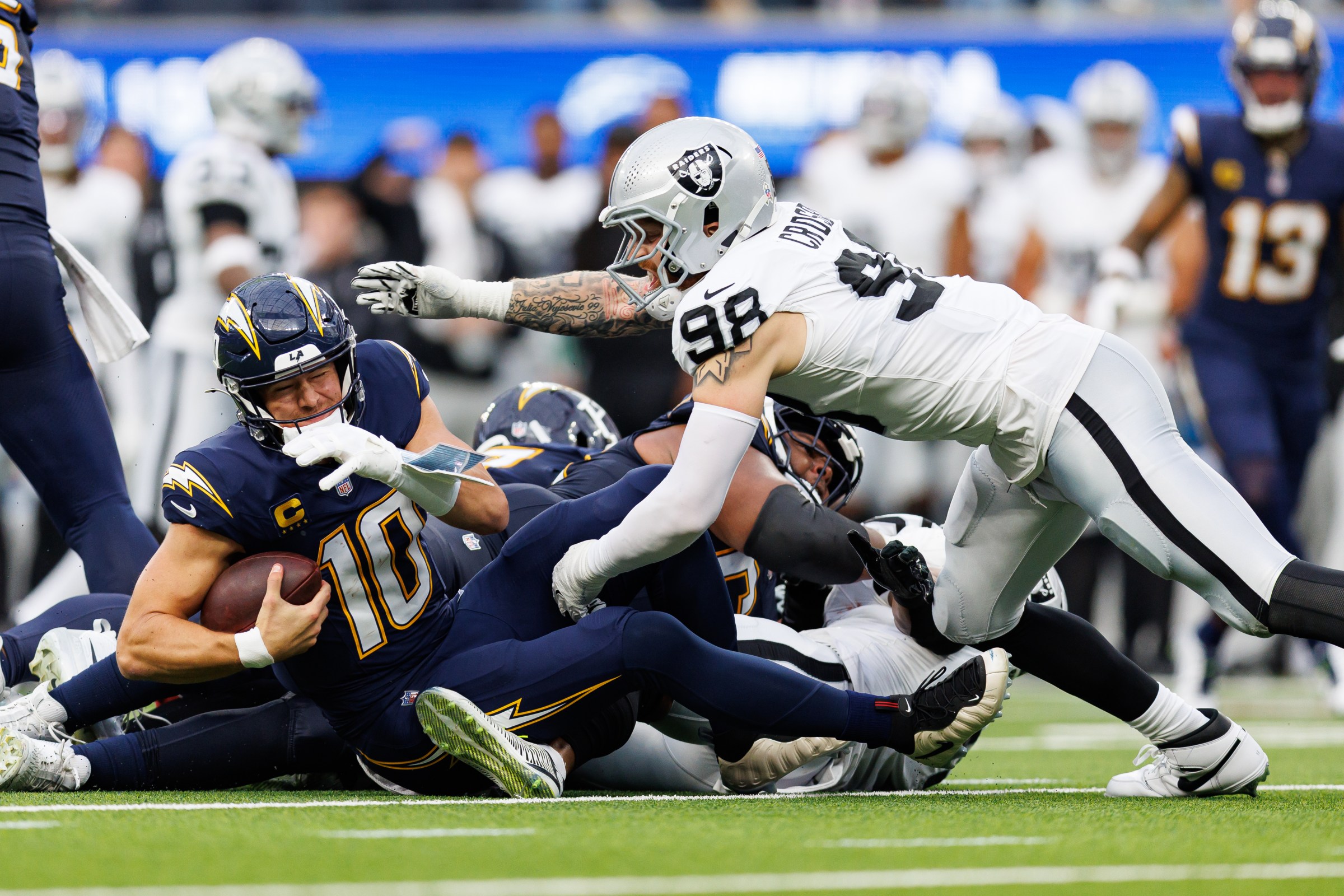 INGLEWOOD, CALIFORNIA - NOVEMBER 30: Justin Herbert #10 of the Los Angeles Chargers is sacked as Maxx Crosby #98 of the Las Vegas Raiders applies pressure during the second half of the NFL football game at SoFi Stadium on November 30, 2025 in Inglewood, California. (Photo by Brooke Sutton/Getty Images)