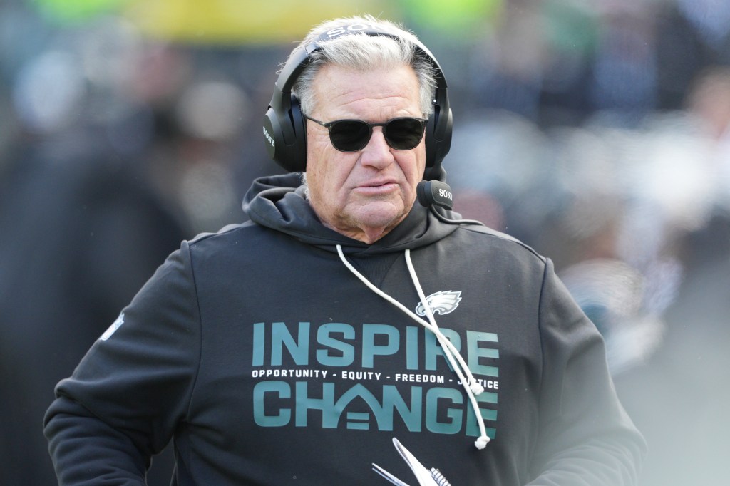 An Eagles coach wears sunglasses and headphones, with an "Inspire Change" hoodie.