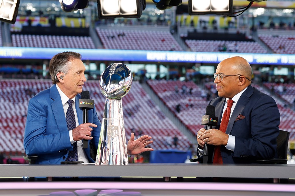 NBC broadcasters Cris Collinsworth and Mike Tirico seated with the Vince Lombardi Trophy between them at Super Bowl LX.