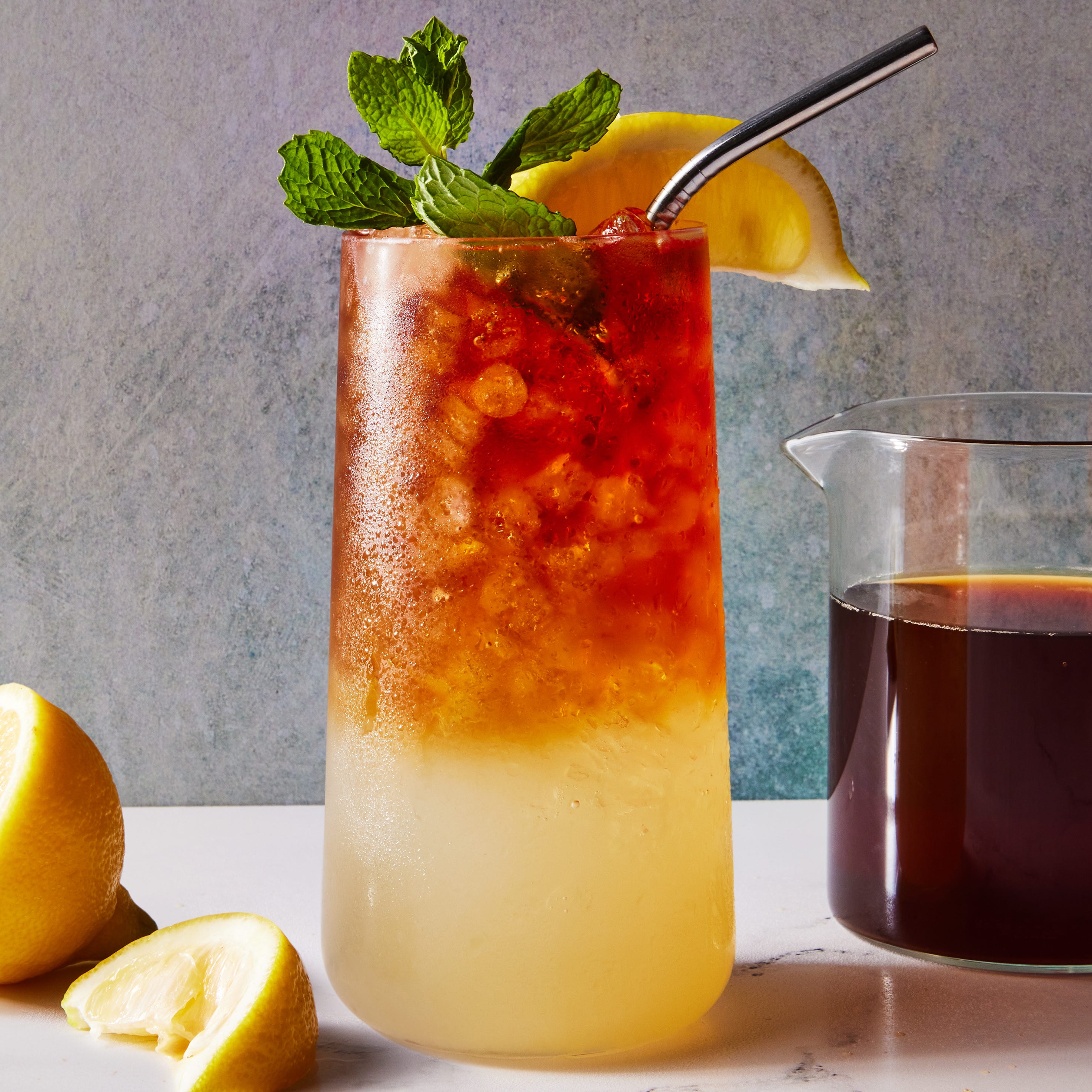 glass with lemonade on the bottom and iced tea on the top with crushed ice, a lemon squeeze and mint