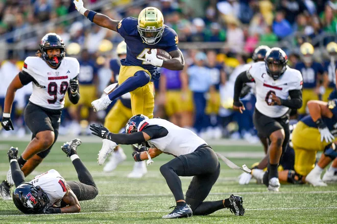 Sep 7, 2024; South Bend, Indiana, USA; Notre Dame Fighting Irish running back Jeremiyah Love (4) jumps over Northern Illinois Huskies safety Nate Valcarcel (9) in the third quarter at Notre Dame Stadium. Mandatory Credit: Matt Cashore-Imagn Images