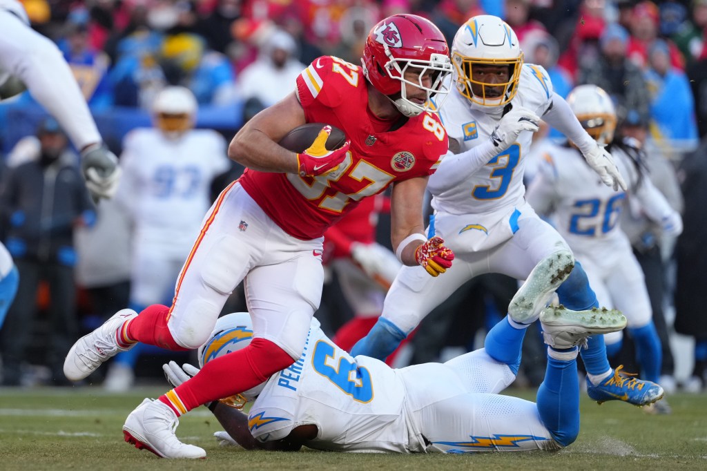 Travis Kelce running with the ball as a Chargers player tackles another player.