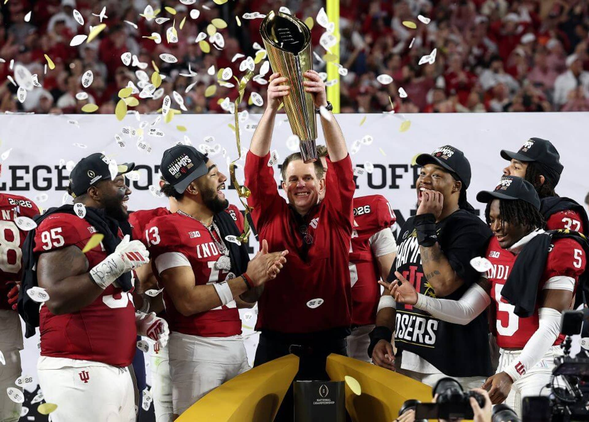 Curt Cignetti holds up the College Football Playoff championship trophy with players around him and confetti falling
