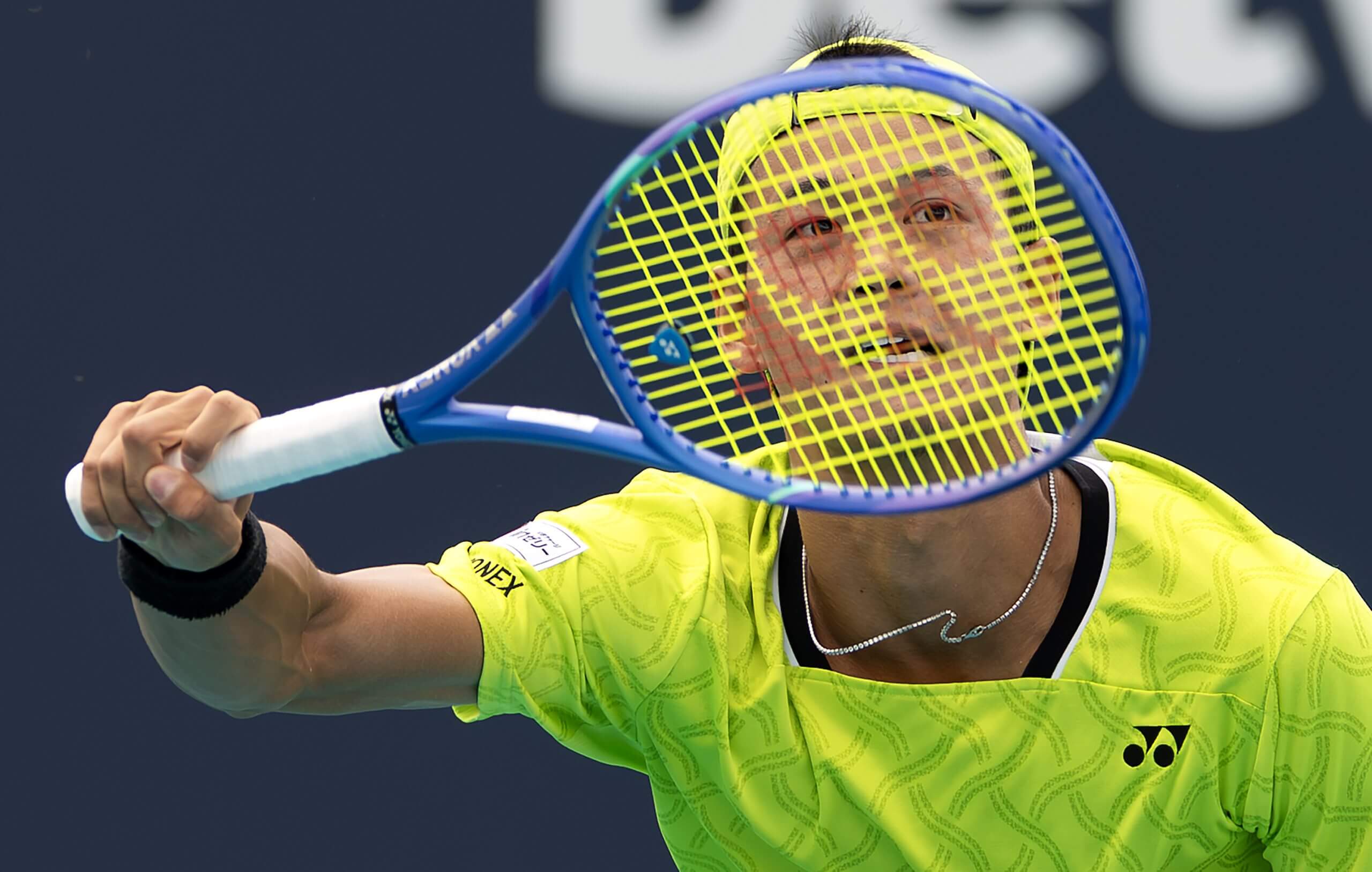 Rei Sakamoto looks through his tennis racket with his eyes and mouth aligning perfectly with its logo.
