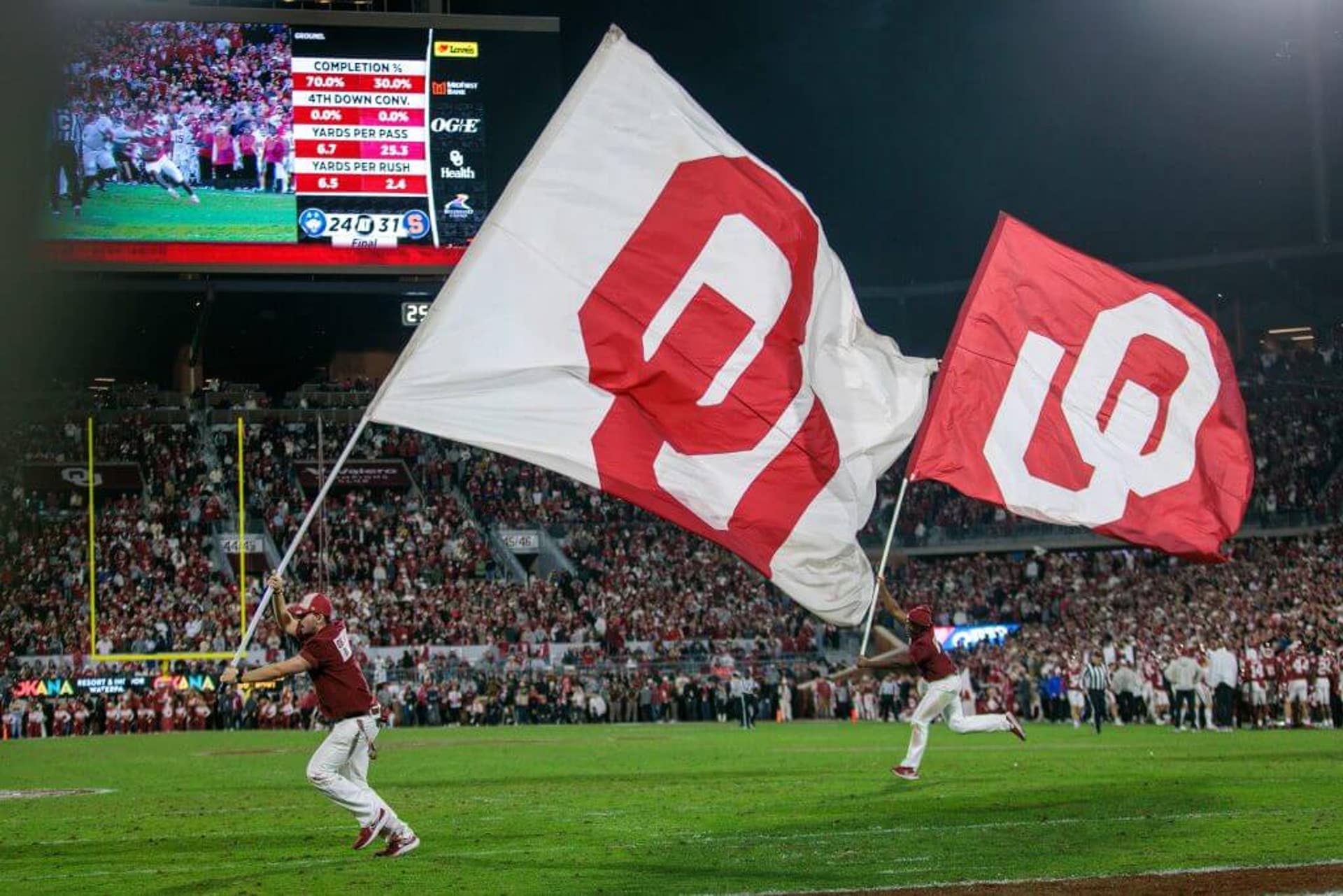 Oklahoma cheerleaders run with OU flags.