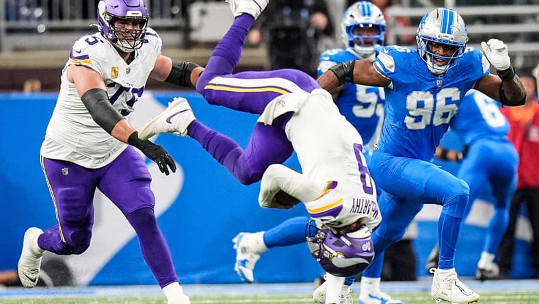 J.J. McCarthy somersaults in the air after a tackle during a Vikings game against the Lions. Vikings rumors