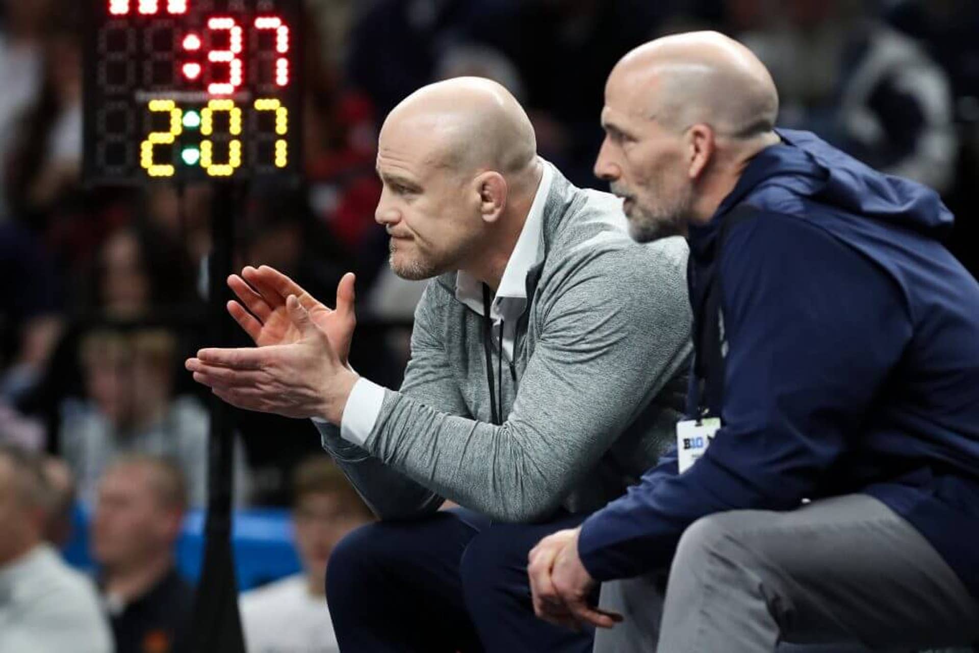Penn State wrestling head coach Cael Sanderson (left) claps while watching one of his Nittany Lions wrestle.