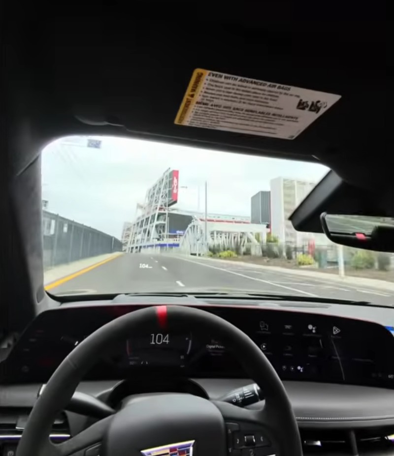 Driver's point-of-view from inside a car showing the speedometer at 104 MPH while driving past a stadium.