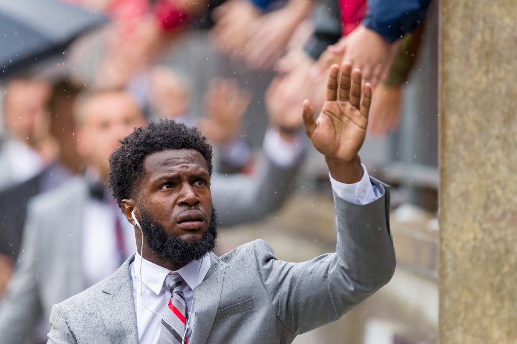 Cornerback Marcus Williamson wearing a suit and earphones while reaching his hand out to greet fans.