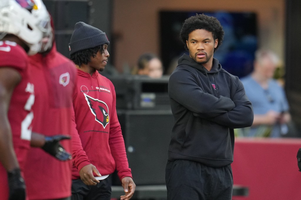 Injured Arizona Cardinals quarterback Kyler Murray, right, looks on as teammates warm up.