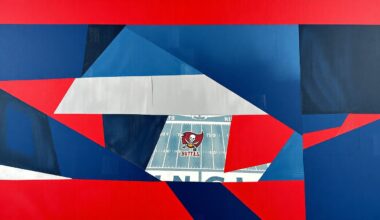 A cubist, geometric painting depicting a fragmented, multi-angled view of a Tampa Bay Buccaneers football game, with sharp planes of navy blue, red, and pewter colors.