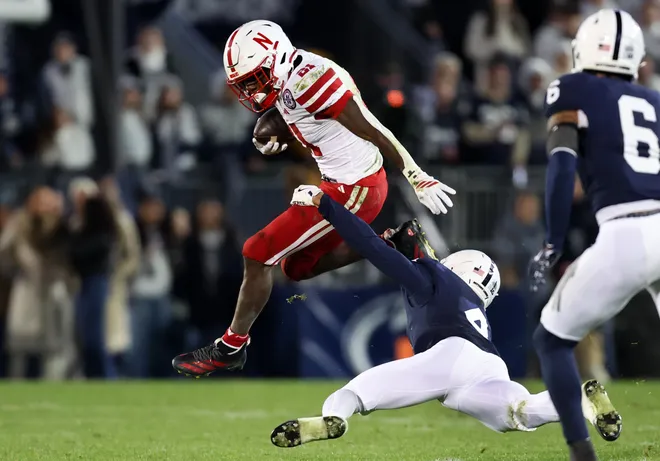 Nov 22, 2025; University Park, Pennsylvania, USA; Nebraska Cornhuskers running back Emmett Johnson (21) jumps to avoid a tackle from Penn State Nittany Lions cornerback A.J. Harris (4) during the first quarter at Beaver Stadium. Mandatory Credit: Matthew O'Haren-Imagn Images