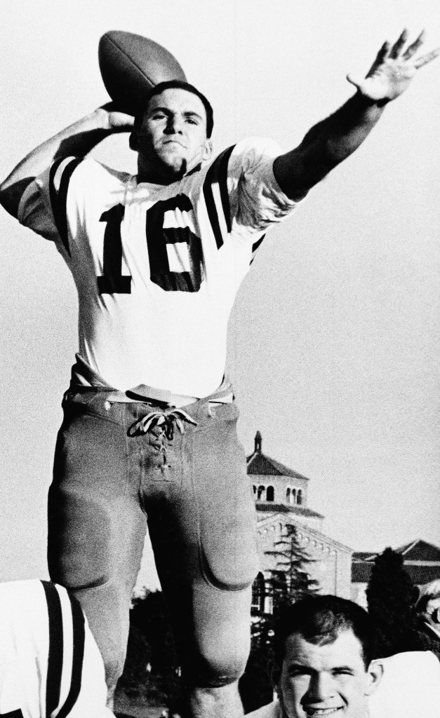 Gary Beban in a football uniform, holding a football and looking up to throw.