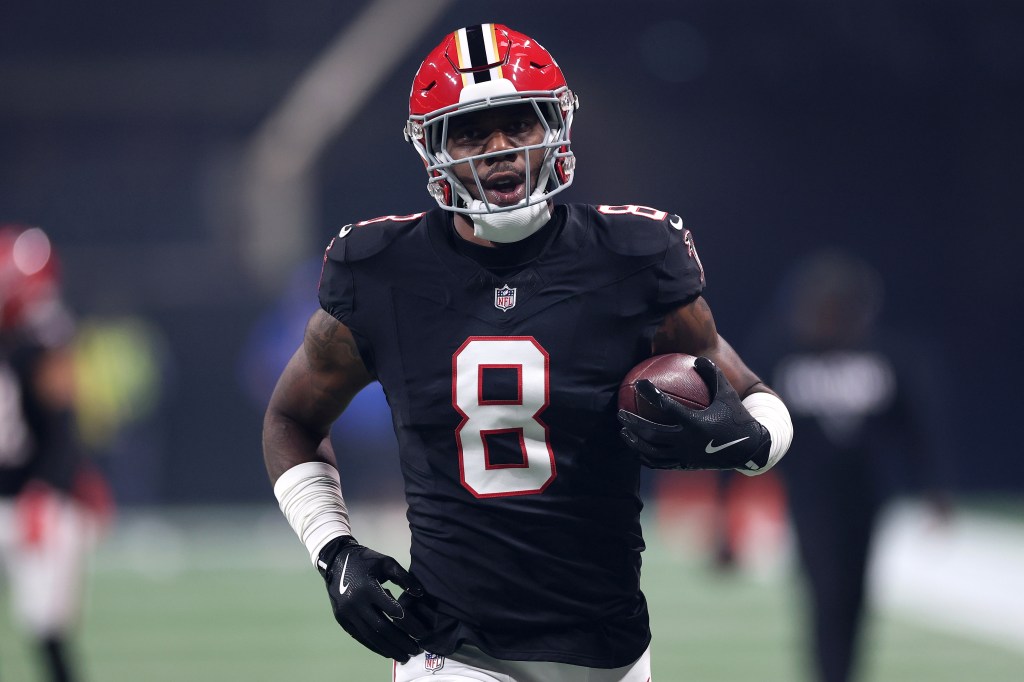 An Atlanta Falcons player in a black jersey with the number 8 and a red helmet runs with the football.