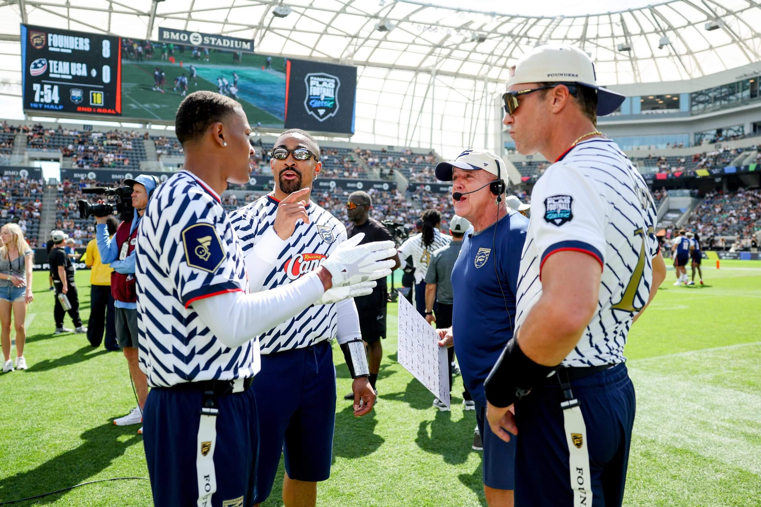 Sean Payton, wearing a headset over his ball cap, stands with flag football players at the Fanatics event.