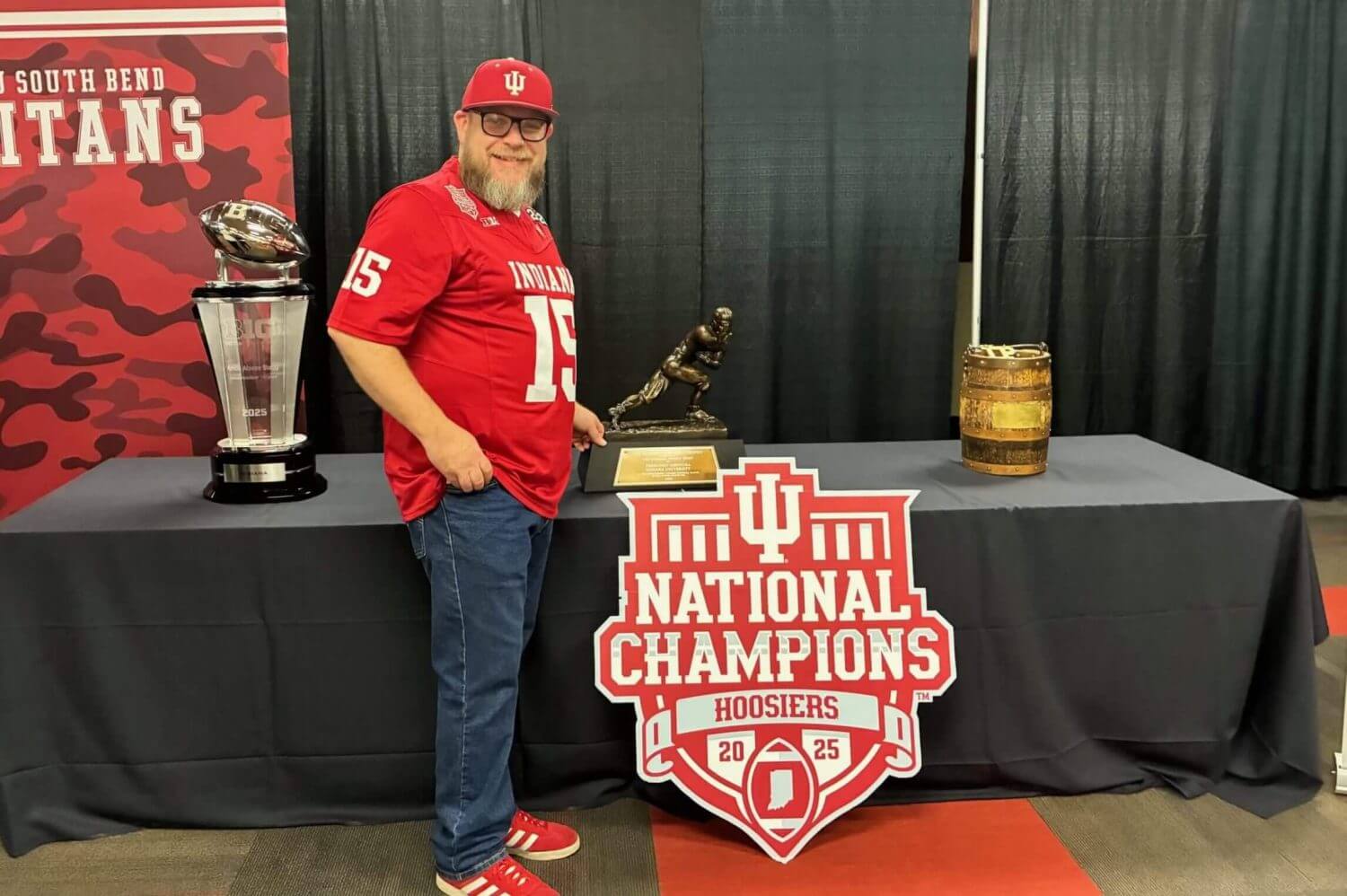 Indiana fan Chris Luchene stands next to the Big Ten championship trophy, the Heisman Trophy and the Old Oaken Bucket..