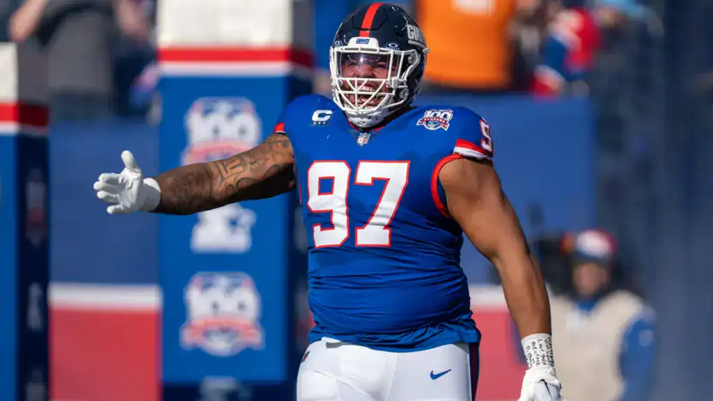 Dexter Lawrence points with a gloved hand while wearing a blue New York Giants helmet on the sideline during a game.