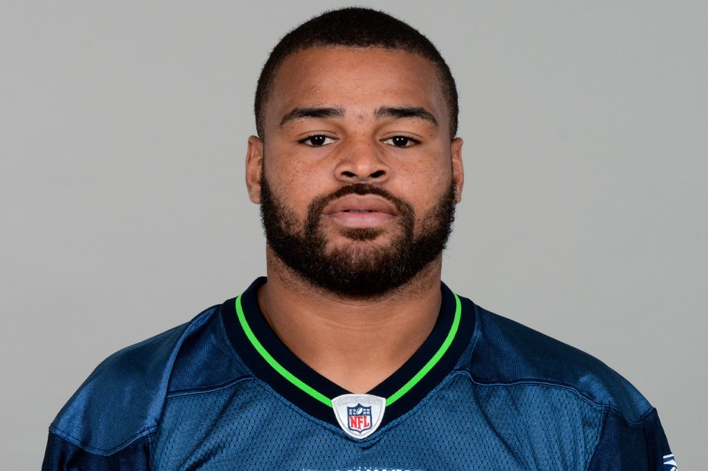 Headshot of a man with a beard wearing a blue and green NFL jersey.