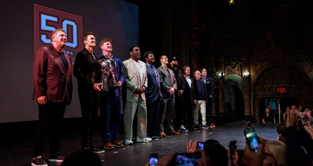 Tampa Bay Buccaneers legends on stage being photographed in Raise the Flags: 50 Years of Buccaneers Football