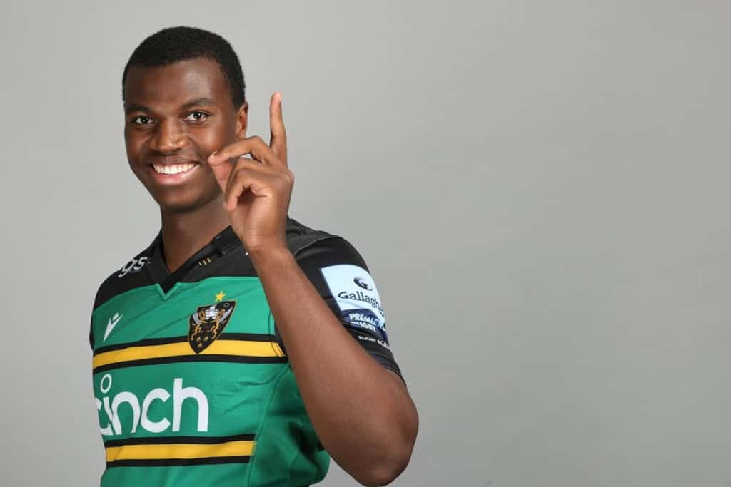 Joshua Weru smiles and points upward while wearing his rugby club jersey, highlighting one of the athletes tied to the NFL International Player Pathway conversation.