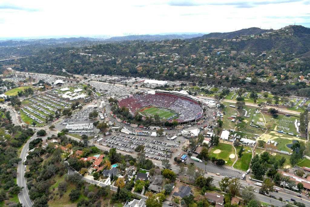 Aerial view of the Rose Bowl, packed with fans, surrounded by parking lots and a hilly landscape.