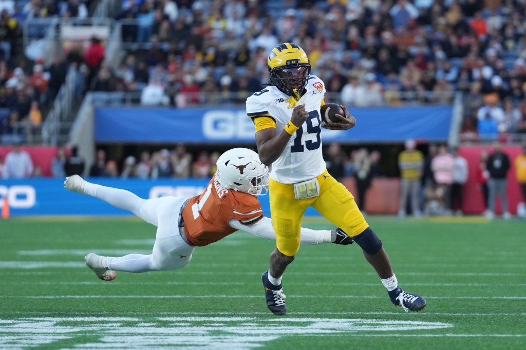 A Michigan player running with the football evades a diving Texas player during the Cheez-It Citrus Bowl.