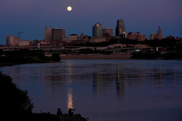  People fish in the Kansas River as the full moon rises beyond the downtown skyline.