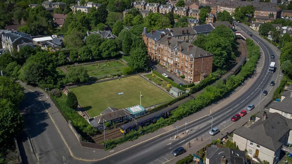 An aerial view of a bowling green with a block of flats and a road running alongside it.