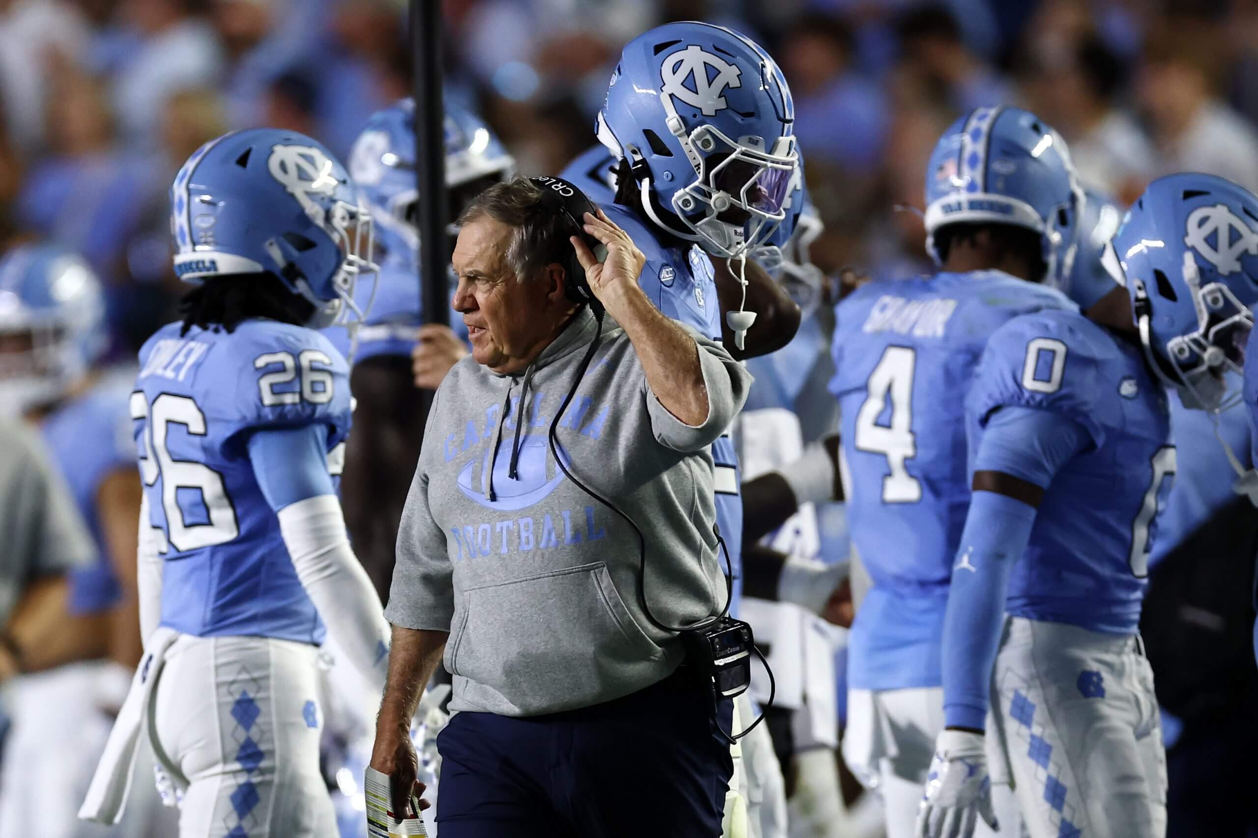 Bill Belichick pulls on his headset while North Carolina players walk behind him