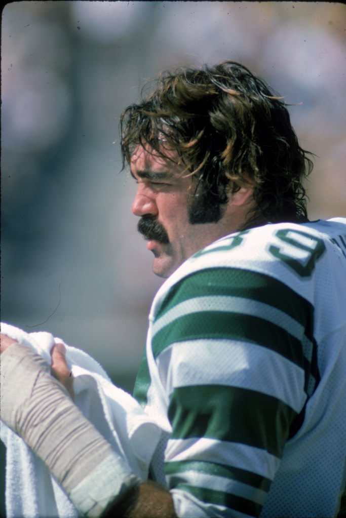 A Philadelphia Eagles player in a green and white striped jersey, with a mustache and sideburns, his hair disheveled, and a bandaged arm.