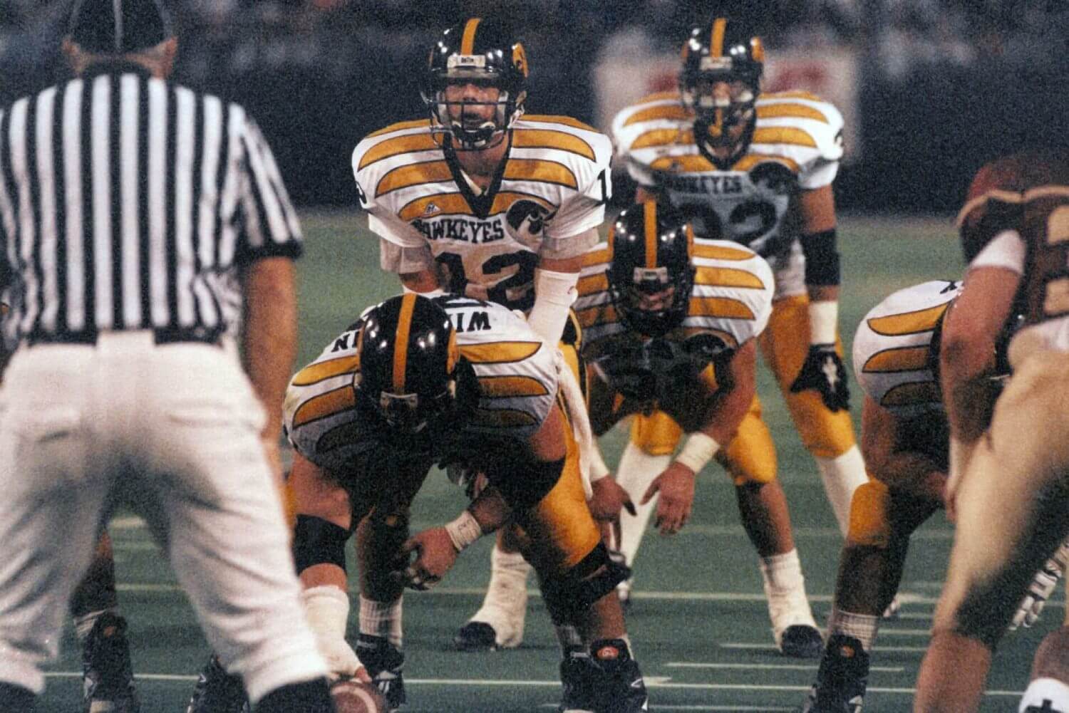 Iowa football players line up wearing white jerseys with tapered yellow bars on the shoulders during a game in the mid-1990s.