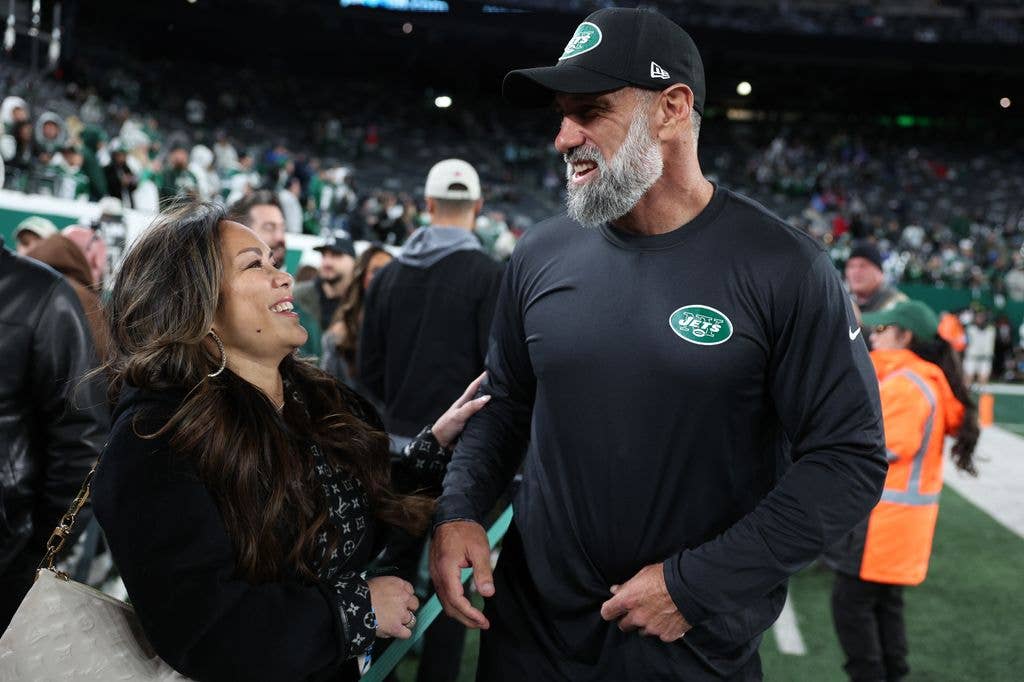 Jeff Ulbrich in Jets cap and shirt talks to smiling Cristina Ulbrich at football game.