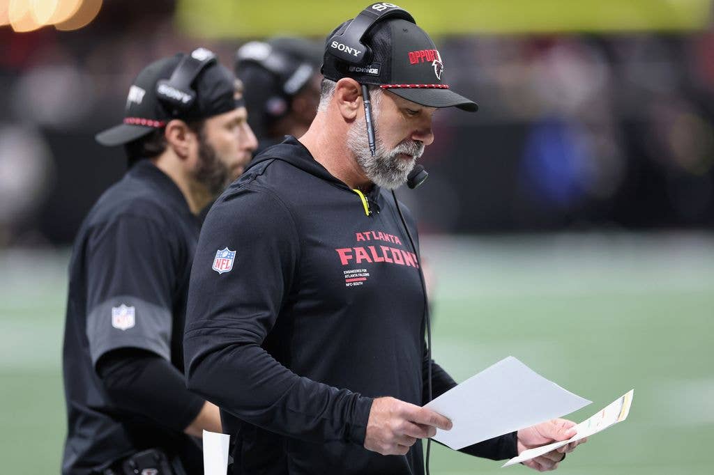 Atlanta Falcons coach Jeff Ulbrich with headset and papers on sideline, another coach nearby.