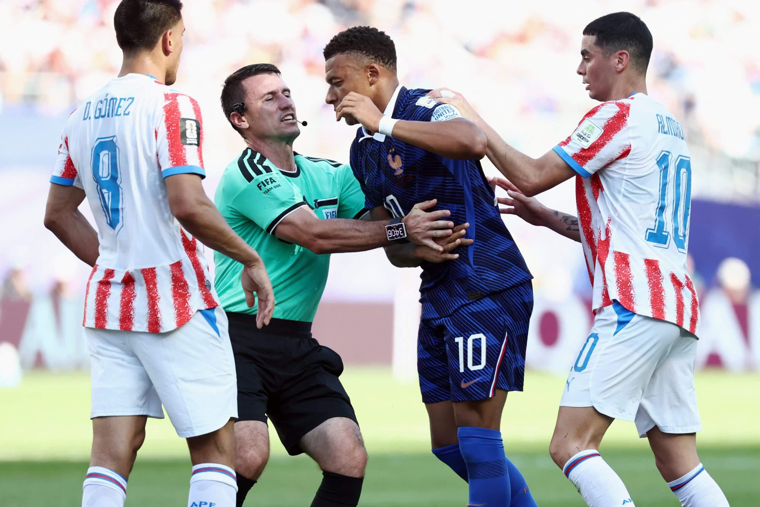 Referee Ilgiz Tantashev holds on to Kylian Mbappe as he clashes with Paraguay's Miguel Almiron