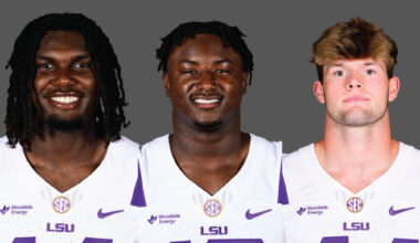 Three LSU football players smiling, wearing white jerseys with purple LSU logos, against a gray backdrop.