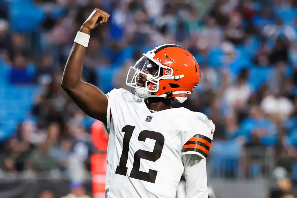 Shedeur Sanders celebrates with a raised fist while wearing his white Cleveland Browns No. 12 jersey.