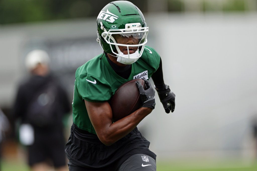 A New York Jets player in a green helmet and jersey runs with a football.
