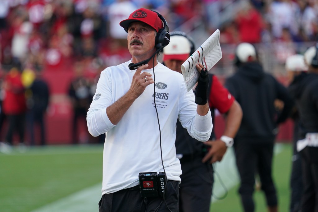 San Francisco 49ers coach in a red cap and headset holding a play sheet.