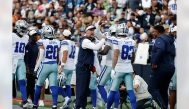 Dallas Cowboys players Malik Davis and Anthony Smith gather on the sideline with coaches during a preseason game.