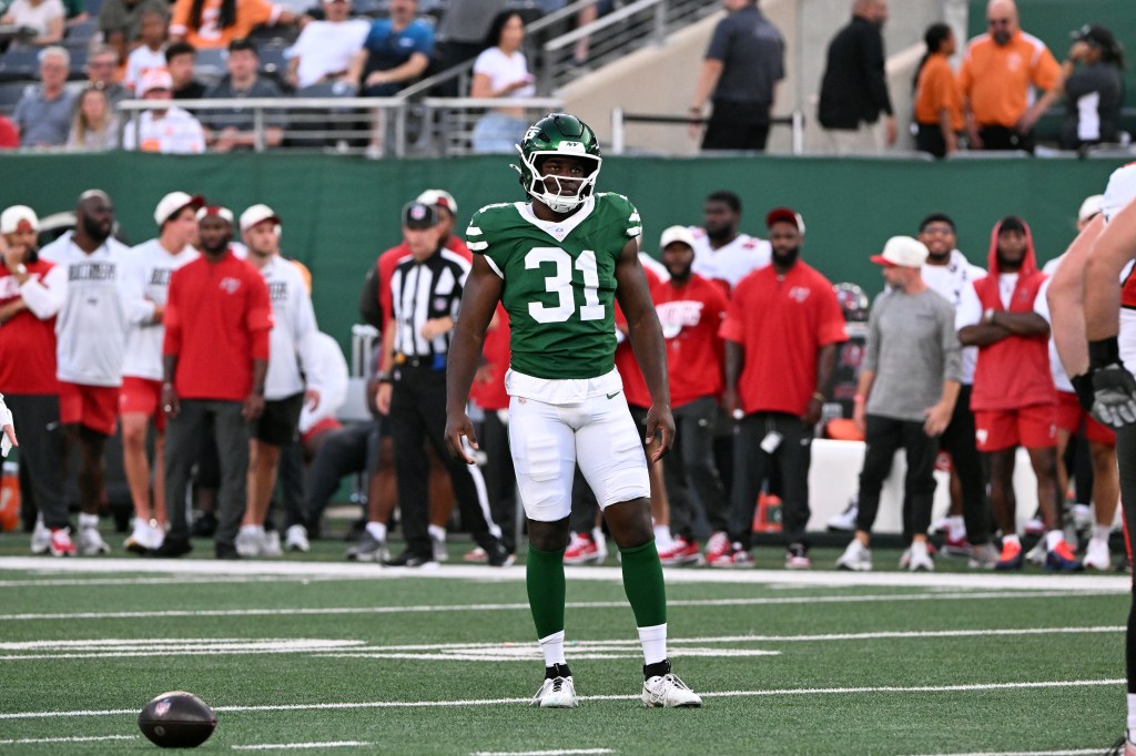 A football player in a green jersey with number 31 stands on a field with a football in the foreground.