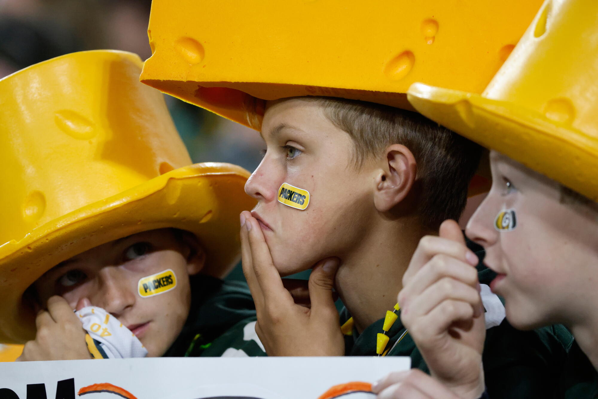 Three young Packers fans in cheeseheads look sad.