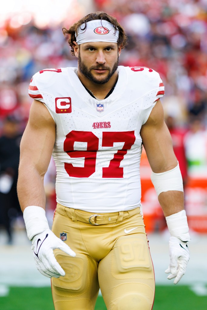 Football player Nick Bosa on the field, wearing a white jersey with red number 97 and tan pants.