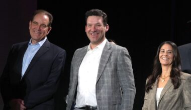 CBS Sports broadcasters Jim Nantz, Tony Romo, and Tracy Wolfson stand together onstage, all smiling.