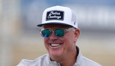 Cowboys chief operating officer Stephen Jones smiles at training camp in a ball cap and sunglasses.