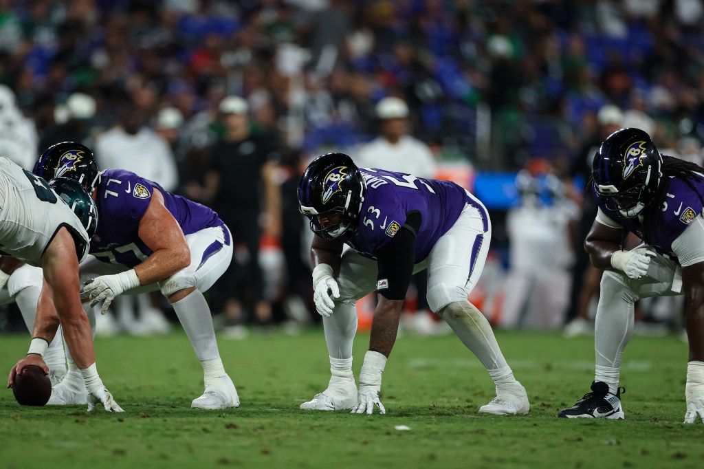 Baltimore Ravens offensive linemen in a three-point stance on the field.