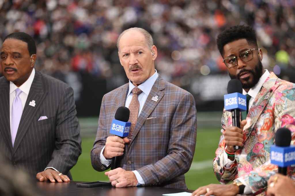 CBS sports broadcaster Bill Cowher speaks into a microphone during halftime, flanked by two analysts.