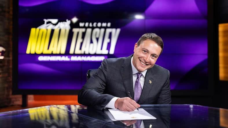 Minnesota Vikings general manager Nolan Teasley signs his contract in front of a "Welcome Nolan Teasley, General Manager" screen.