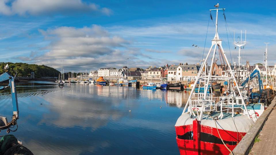 In a picture of Stornoway harbour. A red and white fishing boat is in the foreground. A row of harbour buildings line the waterfront.