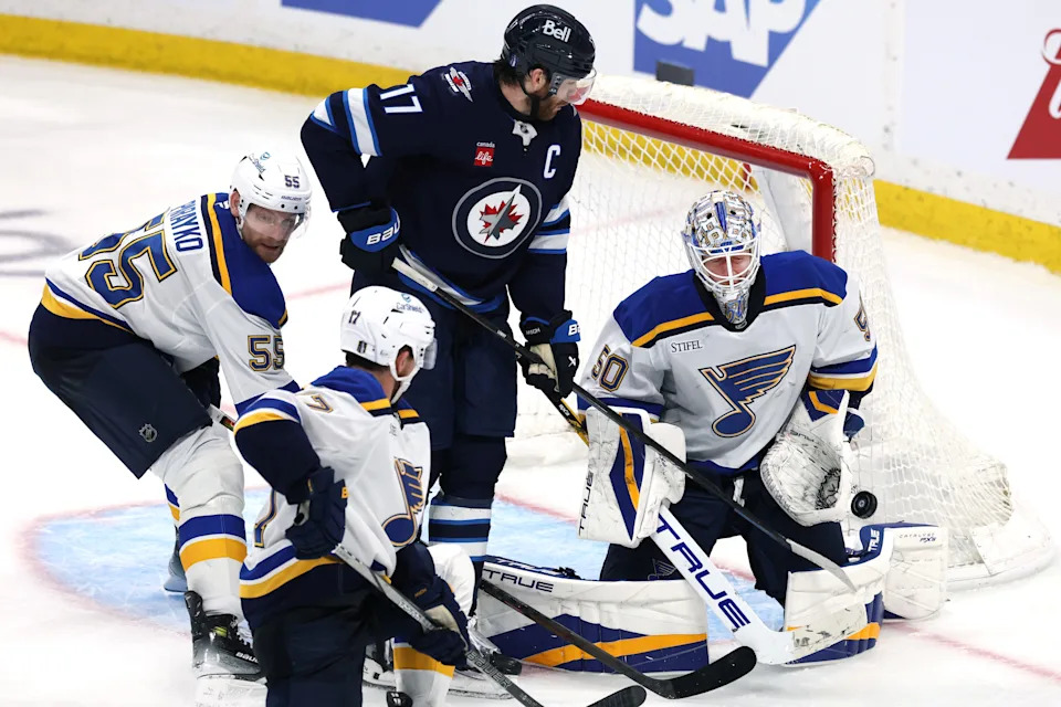 St. Louis Blues goaltender Jordan Binnington (50) makes a save as Winnipeg Jets center Adam Lowry (17) -- the son of former Blues and Peoria Rivermen winger Dave Lowry -- looks for a rebound in OT in Game 7 of the 2025 Stanley Cup Playoffs at Canada Life Centre.