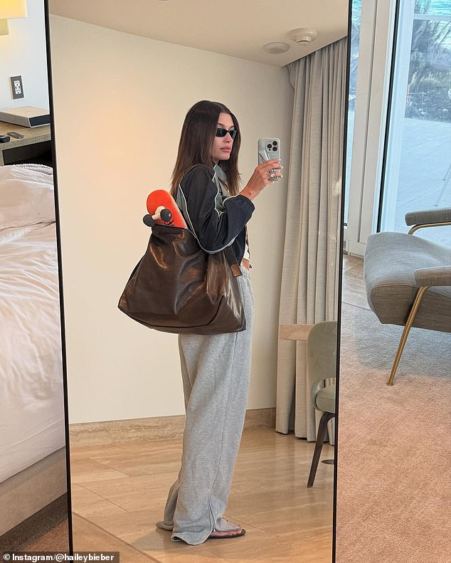 Hailey went ultra-casual in a mirror selfie showing her in a cropped white top, a black-and-ray zip-up jacket and baggie gray sweatpants. She carried an enormous brown bag that a small orange skateboard peeked out of